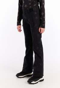 Zwarte skibroek met sterrenpatroon, voorzien van zijritsen, een riem en een licht uitlopende snit, gecombineerd met zwarte laarzen.