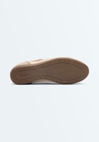 Semelle de chaussure en caoutchouc beige avec motif de la bande de roulement et logo « OYSHO » embossé, vue par le dessous sur un fond uni.