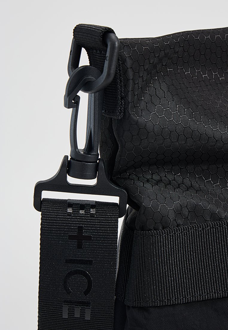Schwarze Tasche aus hexagonal gemustertem Material, ausgestattet mit einem robusten Clip und einem strukturierten Tragegurt, der mit "E + ICE" gekennzeichnet ist. Robuste Bauweise und kompakte Form.