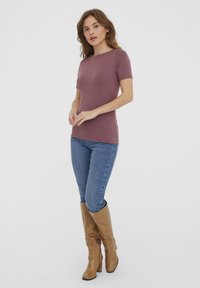 Brun fitted topp med korte ermer parret med blå jeans og beige støvler til knærne. Toppens har rund hals og glatt tekstur.