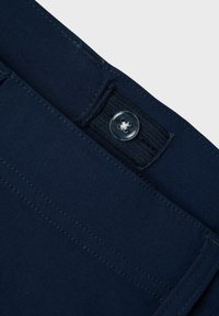 Un tissu bleu marine présente une fermeture à bouton et une ceinture à boucle. Le matériau est lisse avec des coutures visibles le long des bords.