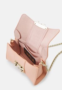 Světle růžová kožená kabelka se zlatým zapínáním, řetízkem a béžovým interiérem obsahujícím přihrádky a štítek Furla.