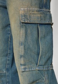 Jeans cargo byxor i ljusblått med synlig sömnad. Har sidofickor och en avslappnad passform, med en urtvättad textur och rekt material.