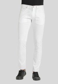 Jeans in denim bianco con una vestibilità slim, dotati di tasche frontali, chiusura con zip e una texture liscia e leggermente lucida. Abbinati a sneakers nere.