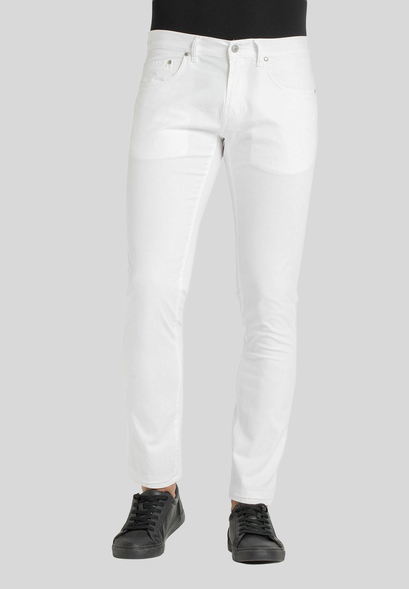 Jeans in denim bianco con una vestibilità slim, dotati di tasche frontali, chiusura con zip e una texture liscia e leggermente lucida. Abbinati a sneakers nere.