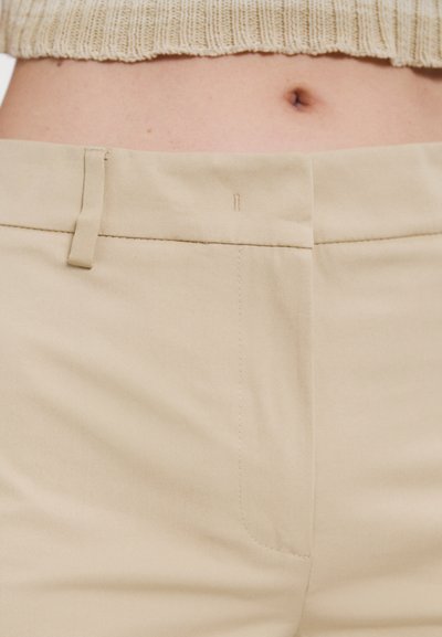 Beige bukser laget av glatt stoff med glidelås og knappefeste. Har side lommer og et rent, minimalistisk design uten mønstre.