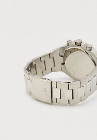 Relógio de aço inoxidável prateado com bracelete de elos, mostrador redondo, botões laterais e acabamento polido na caixa e na bracelete.