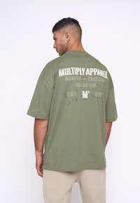 Camiseta verde oliva con un corte relajado, mangas cortas y texto impreso en la parte posterior. El material parece suave con una textura lisa.