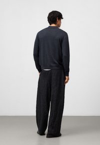 Ciemnoszary, dziany sweter z okrągłym dekoltem i dopasowanymi mankietami, w połączeniu z luźnymi, fakturowanymi czarnymi spodniami. Minimalistyczny design, casualowy krój.