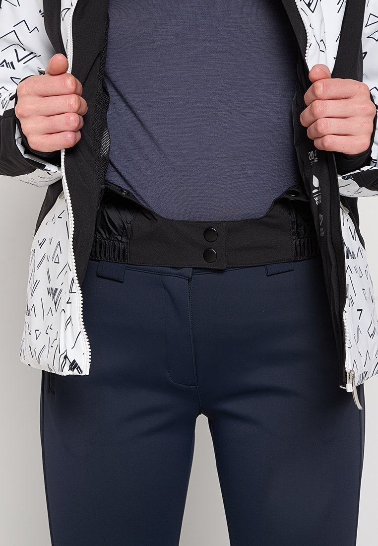 Czarna i biała kurtka w wzory z elastycznym pasem i zapięciem na guziki, w połączeniu z granatowymi dopasowanymi spodniami i szarym podkoszulkiem.