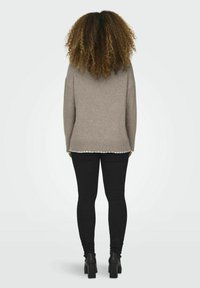 Beige gestrickter Pullover mit geripptem Saum und gewelltem Rand, kombiniert mit schwarzen engen Jeans und Ankle Boots, von hinten betrachtet.