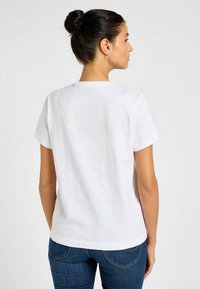 T-shirt bianco a maniche corte con scollo rotondo, texture morbida e vestibilità leggermente rilassata. Abbinato a jeans blu, vista posteriore.