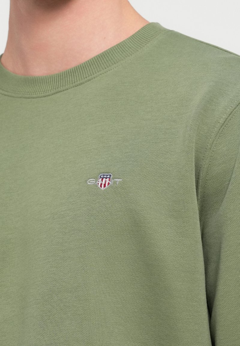 Sweat-shirt en coton vert avec col rond et poignets côtelés. Logo GANT remarquable brodé sur la poitrine en rouge, blanc et bleu.