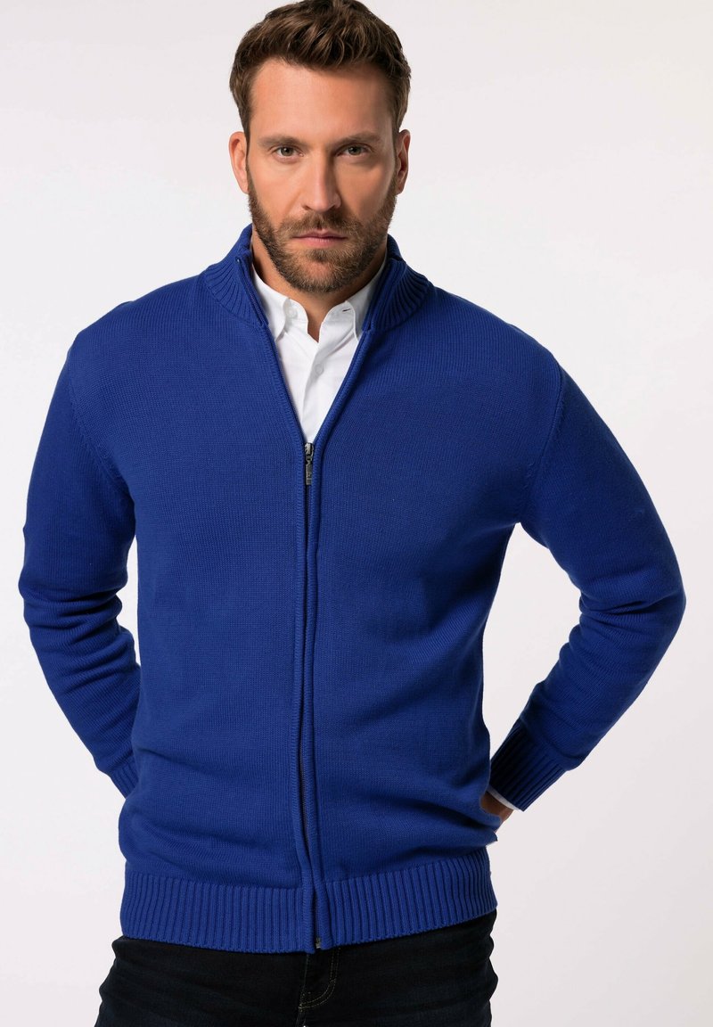 Blauer gestrickter Cardigan mit einem Reißverschluss, gerippten Bündchen und Saum, getragen über einem weißen Hemd mit Kragen und einem hohen Kragen-Design.