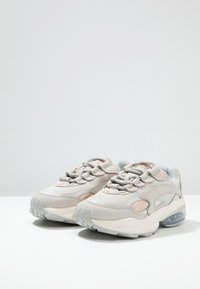 Hellgraue Sneakers aus gemischten Materialien, mit einer strukturierten Oberseite, gepolstertem Schaft, dezenten Akzenten und einer klaren Luftpolstersohle.