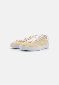 Sneakers in pelle scamosciata gialla chiara con lacci bianchi e suole in gomma. Presentano un design minimale con un logo sul lato.