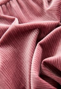 Teksturowany materiał w kolorze mauve z subtelnymi pionowymi żebrami i delikatnym połyskiem, ukazujący łagodne fałdy i draperie. Odpowiedni do różnych zastosowań tekstylnych.