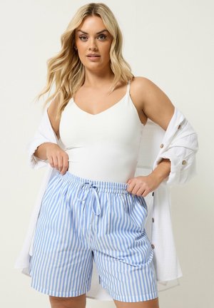 Blondynka ubrana w biały top, białą koszulę na guziki oraz krótkie spodenki w pionowe niebiesko-białe paski z troczkiem w talii.
