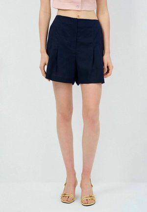 Pantaloni da mare a pieghe blu realizzati in tessuto leggero, con una vita pulita e una vestibilità su misura, abbinati a sandali chiari con cinghie.