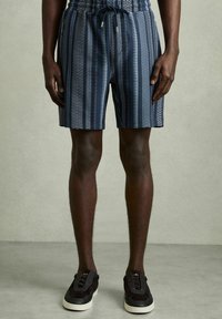 Mønstret shorts i navy med lodrette striber og zigzag-design. Elastisk talje med snor. Sammen med sorte sneakers.