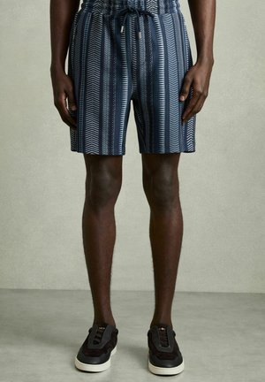Patterned shorts in navy with vertical stripes and zigzag design. Elastic waistband with drawstring. Paired with black sneakers.