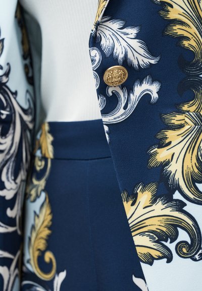 Προσαρμοσμένο μπλε σακάκι με χρυσά και λευκά μπαρόκ φύλλα, με διακοσμητικό χρυσό κουμπί και ταιριαστό σκούρο μπλε παντελόνι με ψηλή μέση.