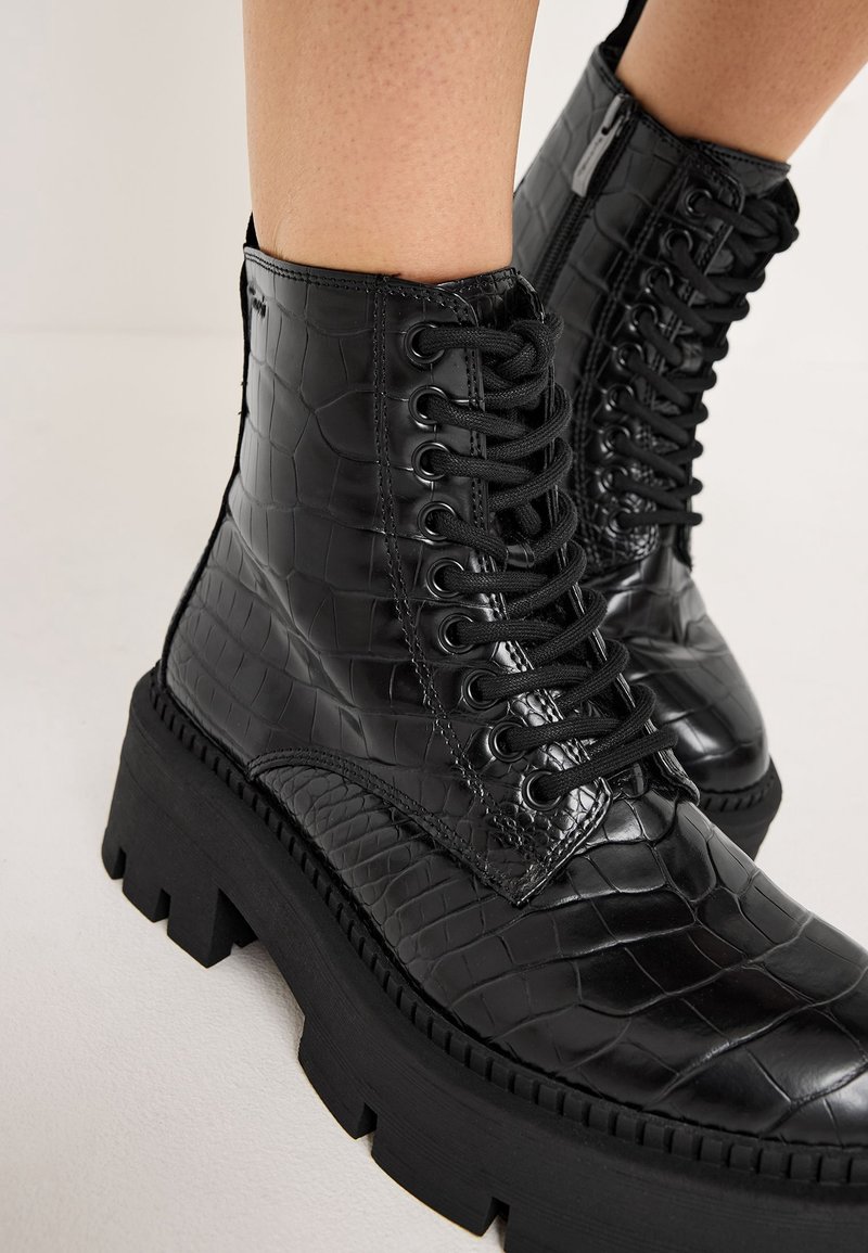 Bottes noires à cheville avec texture croco, dotées d'une semelle épaisse haute, d'un laçage à l'avant et d'une fermeture éclair latérale. Finition lisse et brillante.