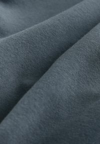 Tejido gris suave con una textura lisa, que presenta finos hilos entrelazados. El material parece ligero y cae de manera suelta en pliegues.