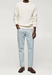 Cremefarbener, kabelgestrickter Pullover, hellblaue Jeans mit geradem Schnitt und braune Loafers. Der Pullover hat gerippte Bündchen und Saum. Die Jeans verfügen über Standardtaschen.