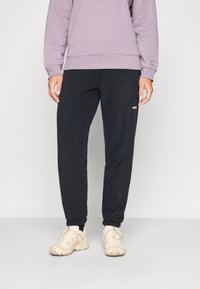 Black athletic pants with elastic cuffs, lightweight fabric, and side pockets, paired with a lavender sweatshirt and beige sneakers.