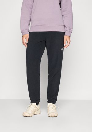 Schwarze Sporthosen mit elastischen Bündchen, leichtem Stoff und seitlichen Taschen, kombiniert mit einem lila Sweatshirt und beigen Sneakers.