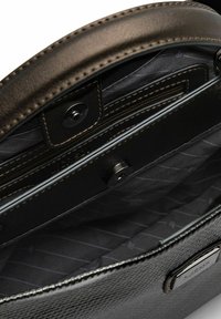 Interno di una borsa a tracolla in pelle nera con una fodera chiara, caratterizzata da una chiusura magnetica, tasche e dettagli di cucitura.