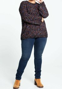 Mörk, texturerad tröja med flerfärgade prickar, parat med slim-fit mörka jeans och bruna ankelstövlar med klack.