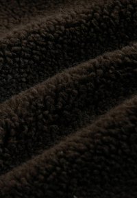 Tumepruun, tekstuuriga kangas, millel on karvane, sametine pind tihedatest kiududest, mis on paigutatud kihilistesse voldikutesse ja loovad pehme mulje.