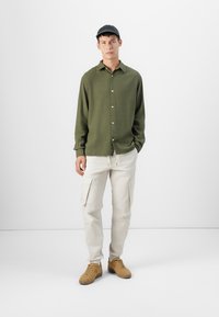 Long-sleeve olive green shirt with buttons, paired with beige cargo pants featuring side pockets and tan sneakers.