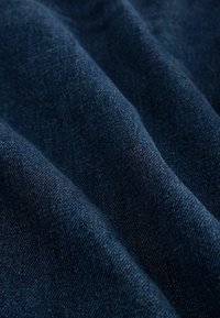 Tela de mezclilla azul oscuro con una textura suave, que muestra variaciones sutiles en el tejido y el sombreado, destacando su caída flexible y suave.