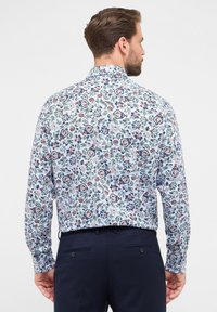 Camicia a maniche lunghe con sfondo bianco e motivi floreali colorati in rosso, blu e verde. Colletto classico e polsini con bottone.