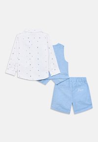 Valkoinen pitkähihainen paita, jossa monivärisiä geometrisia kuvioita; siniset shortsit, joissa joustava vyötärö ja kirjailtu logo. Rakenne on teksturoitu ja rento.