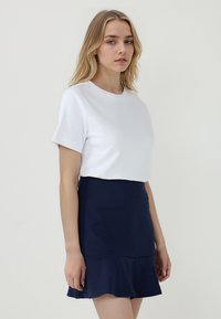 Witte top met korte mouwen en ronde halslijn, gecombineerd met een marineblauwe uitlopende rok, die een gladde textuur en een aansluitende taille heeft.