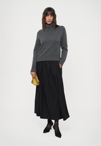 Grå høyhalset genser, svart lang plisserte skjørt, svarte strømpebukser, svarte høye hæler, holder en liten gullhåndveske. Enkelt, elegant antrekk.