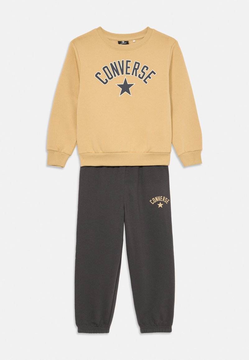 Sweatshirt amarelo com o texto "CONVERSE" e logótipo de estrela, combinado com calças de moletão cinzas com bordado do logótipo. Ambos feitos de tecido macio.