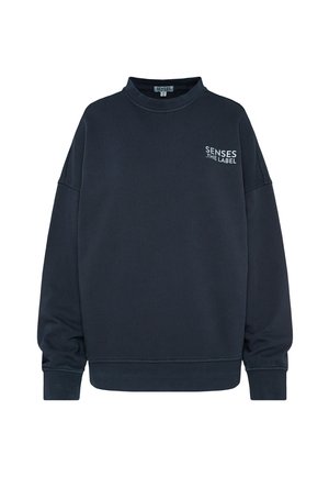 Marineblaue Sweatjacke aus weichem Stoff, mit hohem Kragen, überschnittenen Schultern und einem kleinen weißen Logo auf der Brust.