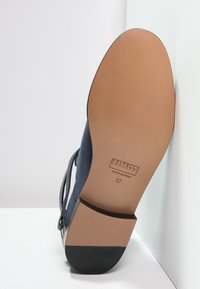 Suela de un zapato de cuero azul marino con suela de color marrón suave, punta del tacón negra y etiqueta de tamaño 37 que dice "Fratelli Rossetti Hecho en Italia."