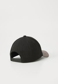 Casquette noire avec une visière grise, en tissu. Présente une visière plate et une fermeture réglable à l'arrière. Surface texturée visible.