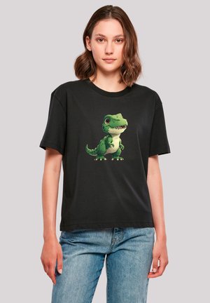 Young woman wearing black t-shirt with cartoon green dinosaur on front, paired with blue jeans, standing against plain light background.