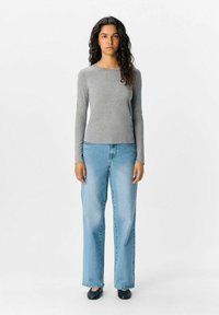 Grå langærmet bluse parret med lyseblå brede bukser og sorte sko. Stoffet er blødt, med en glat tekstur og et simpelt design.