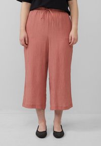 Pantalons légers, plissés et cropped en rose poussiéreux avec une taille à cordon et une coupe droite, associés à des ballerines noires ornées.