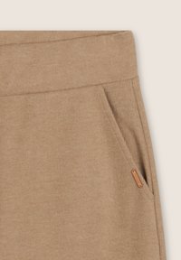 Pantalones deportivos beige con textura acanalada, bolsillos laterales y una pequeña etiqueta de cuero en la cintura, con una textura suave y cinturilla elástica.