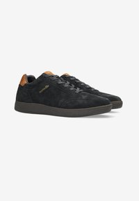 Sneaker in suede nero con inserto in pelle marrone sul tallone, con lacci piatti e suola in gomma testurizzata. Logo dorato lungo il lato.