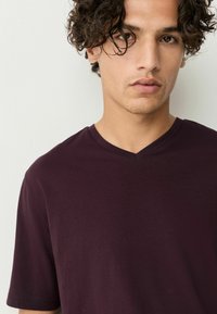 Burgundy V-ringad t-shirt i mjukt, slätt tyg med korta ärmar, med en avspänd passform och minimala sömnadsdetaljer.